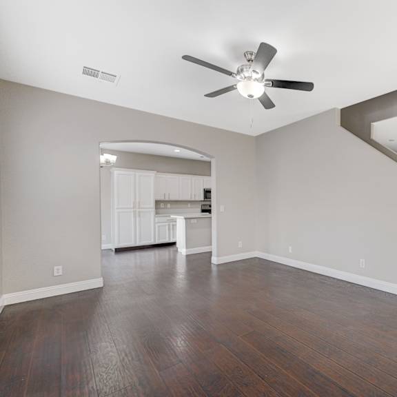an empty living room with a ceiling fan and a kitchen