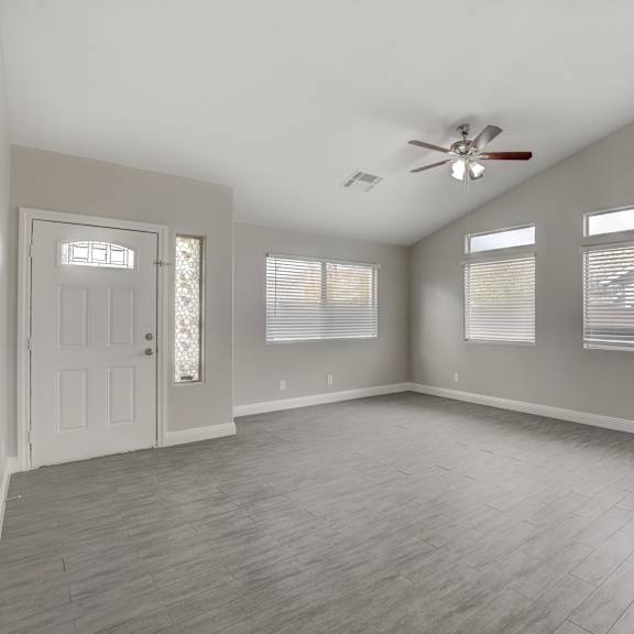 a room with a ceiling fan and three windows.