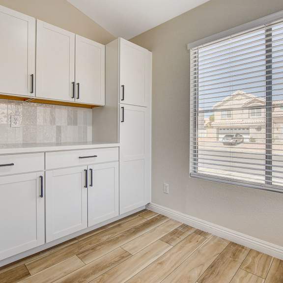 a kitchen with white cabinets and a window with blinds.