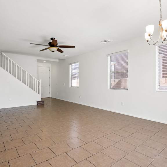 an empty living room with a ceiling fan and a staircase