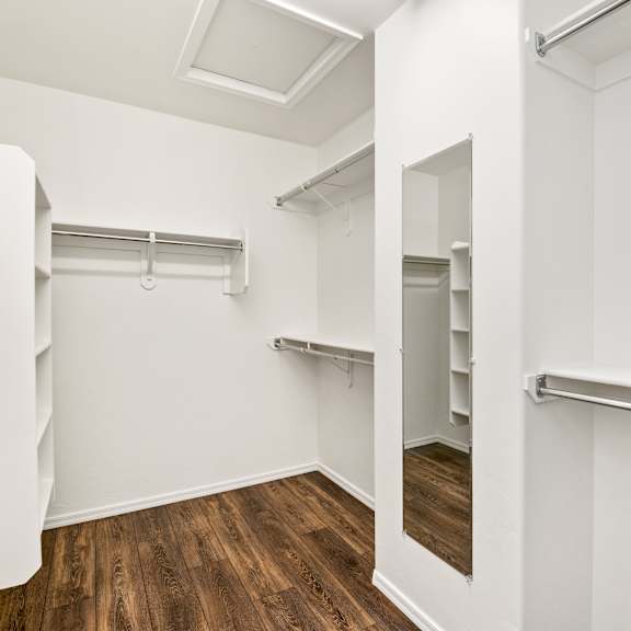 a walk in closet with white walls and wood flooring