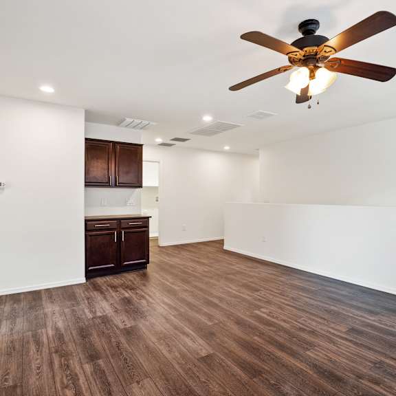an empty living room with a ceiling fan and a kitchen