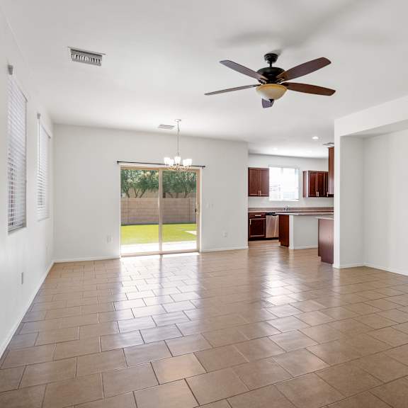 an empty living room with a ceiling fan and a kitchen