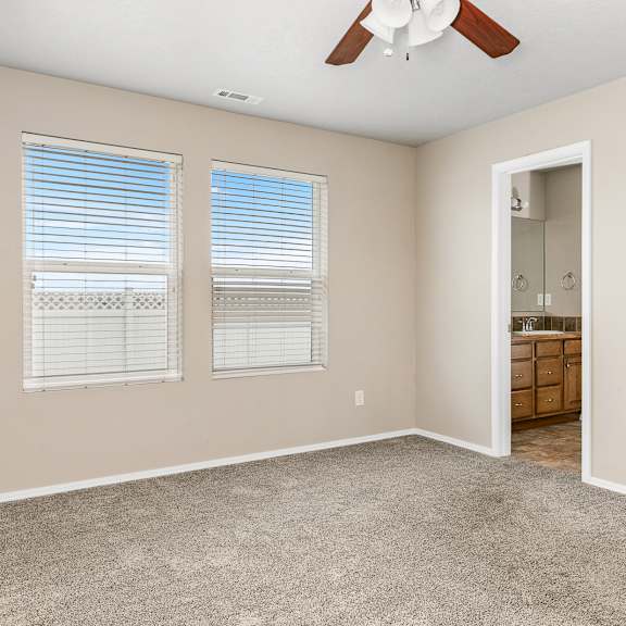 a room with a ceiling fan and two windows.