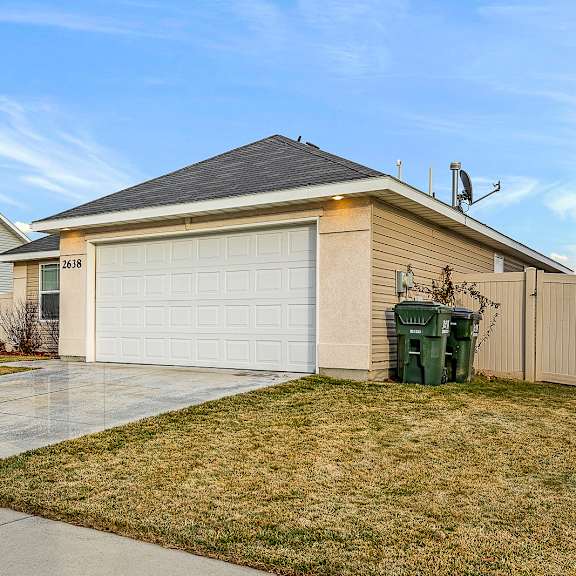 a house with a white garage door and a green trash bin in front.