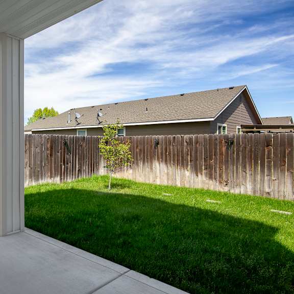 a white pillar stands in a concrete patio with a wooden fence and houses in the background.