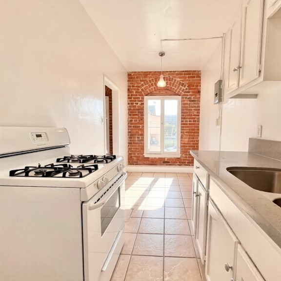a kitchen with a white stove, white cabinets, and a brick wall.
