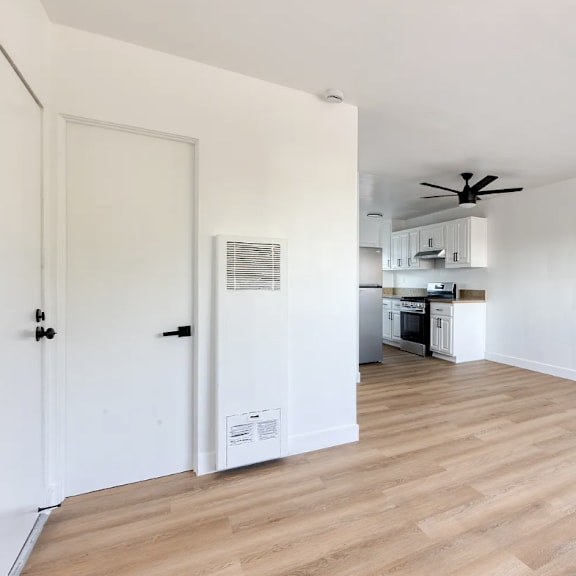 a room with a ceiling fan and a kitchen area in the background.