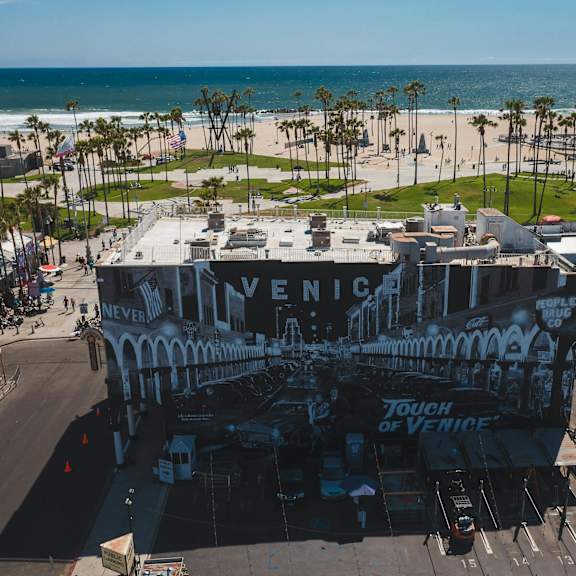 a large building with a mural on the side is in the foreground of a beachfront area.