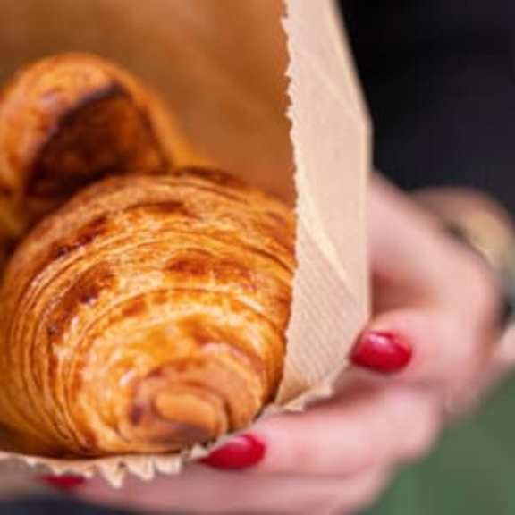 a person holding a paper container filled with croissants.