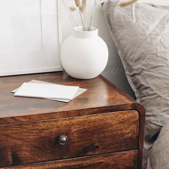 a wooden nightstand with a cup of coffee and a book on top of it.
