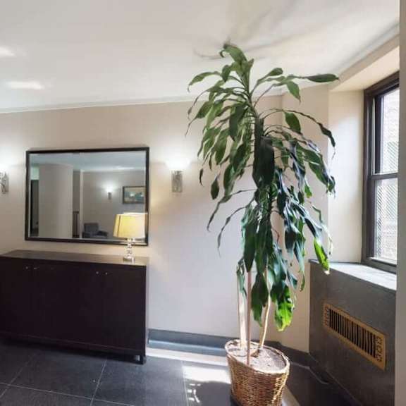 a room with a grey chair, a mirror, a lamp, and a plant.