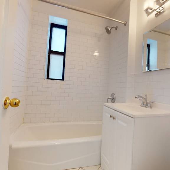 a white bathroom with a tub, sink, mirror, and a window.