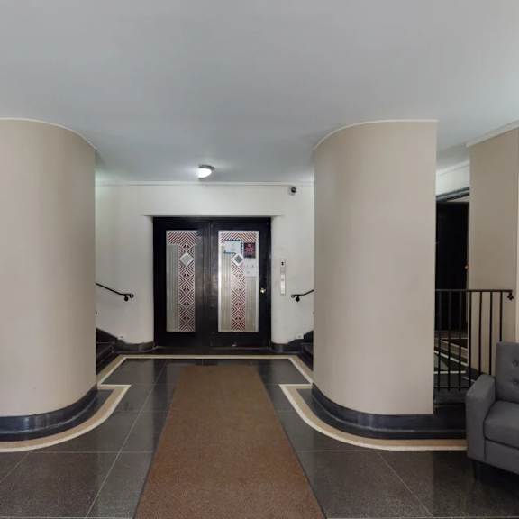 a hallway with a brown carpet and two grey armchairs.