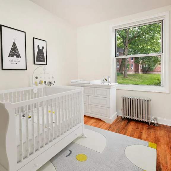 a white crib sits in a room with a grey rug and three pictures on the wall.