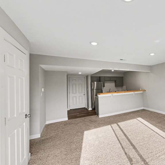 a spacious room with a carpeted floor and a bar area in the background.