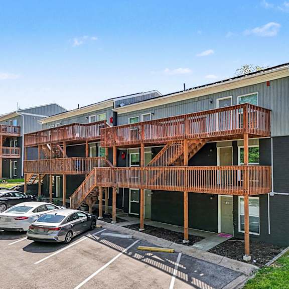 a parking lot with cars and a building with a balcony.