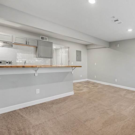 a spacious room with a kitchenette and beige carpeting.