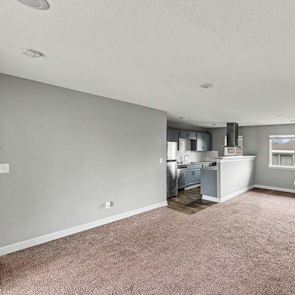 a spacious living room with a kitchen in the background.