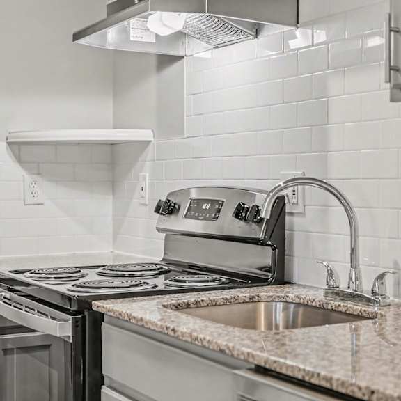 a kitchen with a stove, sink, and a white tile backsplash.