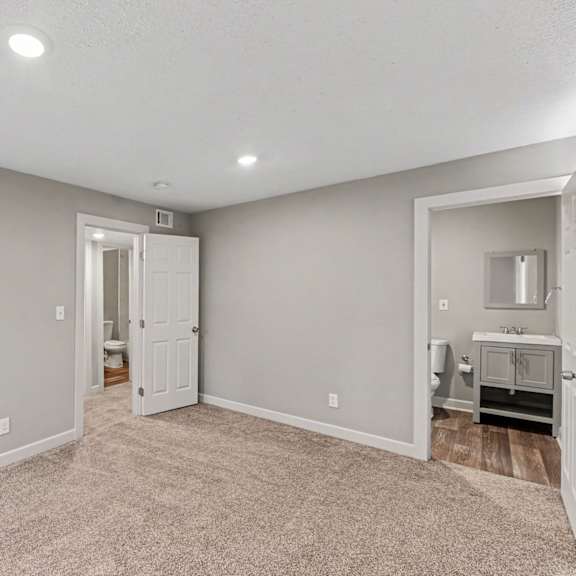 a spacious room with a carpeted floor and a kitchenette in the corner.