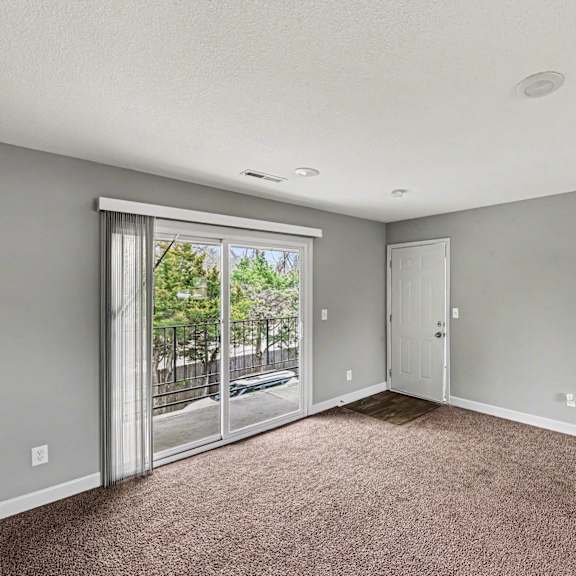a room with a carpeted floor and a sliding glass door leading to a balcony.