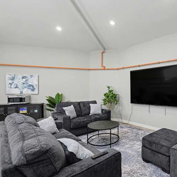a living room with grey couches and a flat screen tv mounted on the wall at mayfair apartments, kansas city, mo, 64145