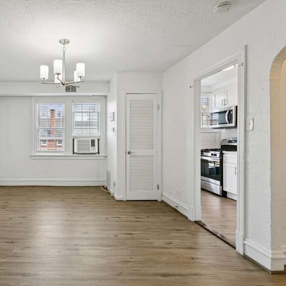 a large empty room with a chandelier and a kitchen in the background. at shipyard shores apartments, newport news, 23607