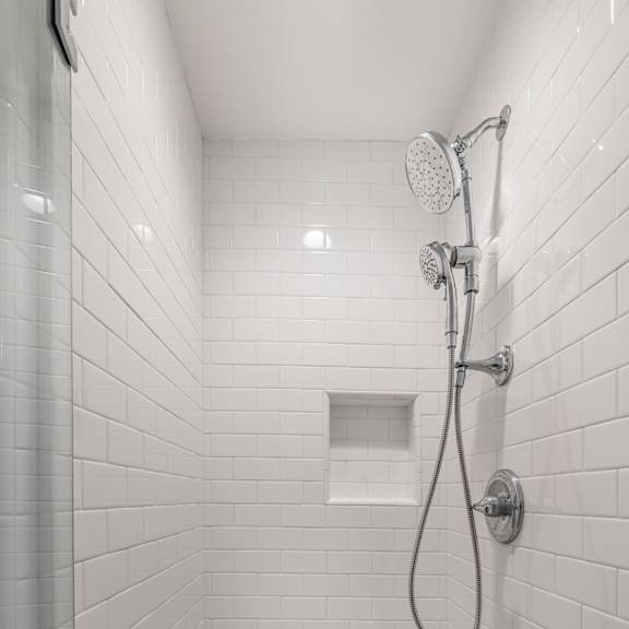 a white tiled shower with a shower head and hand held shower.