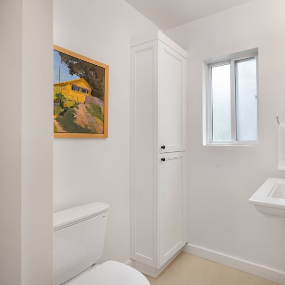 a white bathroom with a toilet, sink, and a painting on the wall.