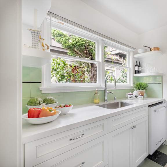 a kitchen with a white counter top and a window with plants on it.