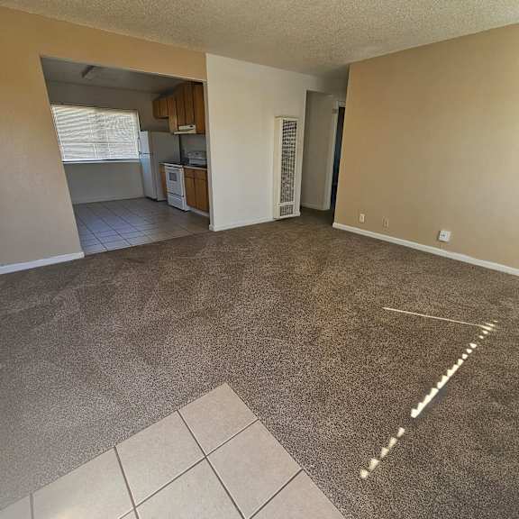 Thumbnail 2 of 14 an empty living room with a kitchen in the background