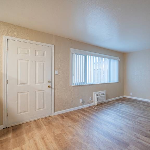 Thumbnail 2 of 18 A room with a white door, a window with blinds, and a wooden floor.