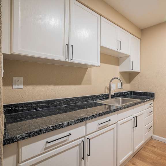Thumbnail 1 of 18 A kitchen with white cabinets and a black countertop.