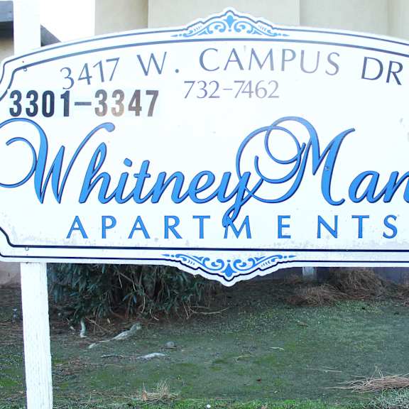 a sign for whitney manor apartments is displayed in front of a building.