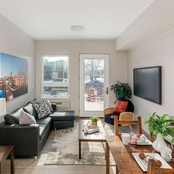 a living room with a black couch, a wooden coffee table, and a large window.