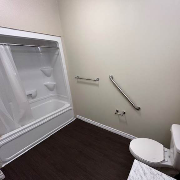 a small bathroom with a toilet, a shower with a glass door, and a grab bar.