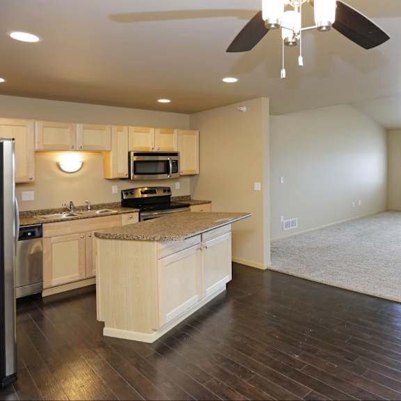 a spacious kitchen with wooden floors and a ceiling fan.