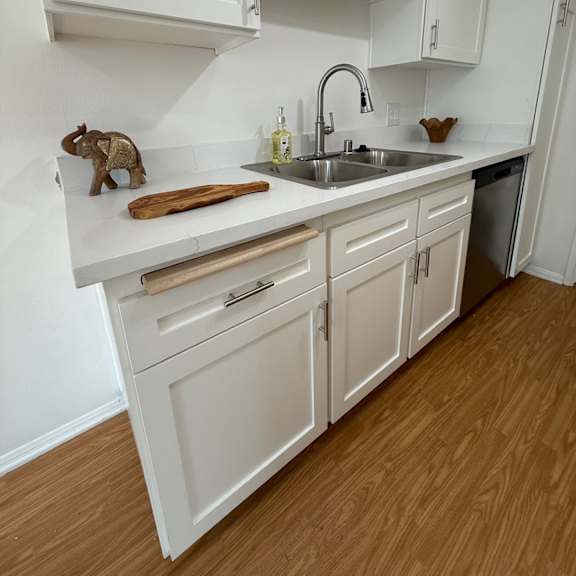 Thumbnail 4 of 6 A kitchen with white cabinets and wooden floors.