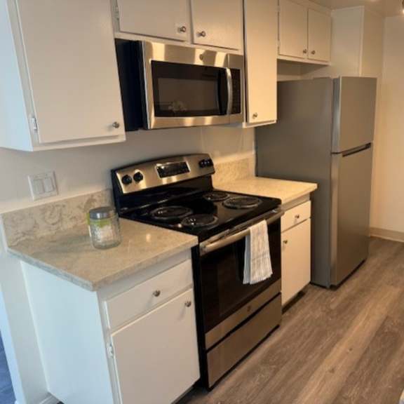 Thumbnail 3 of 4 A kitchen with a stove, refrigerator, and microwave.