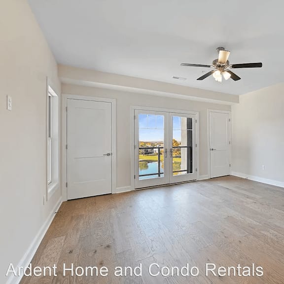 an empty living room with a ceiling fan and a door to a balcony