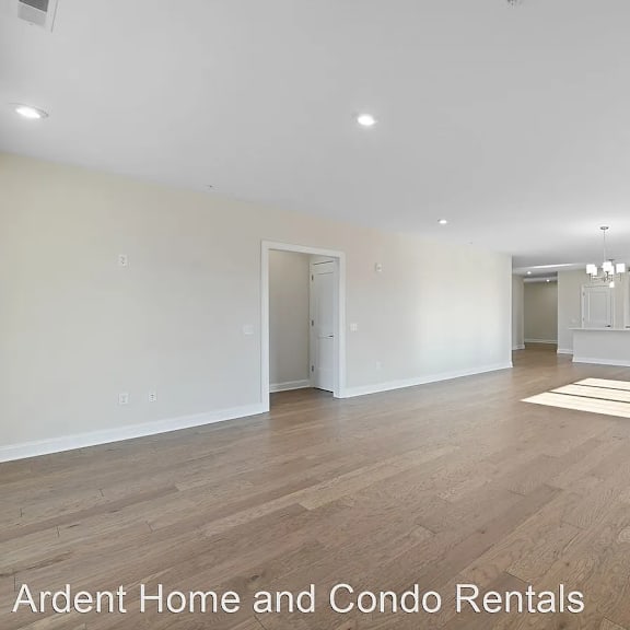 an empty living room with a kitchen in the background