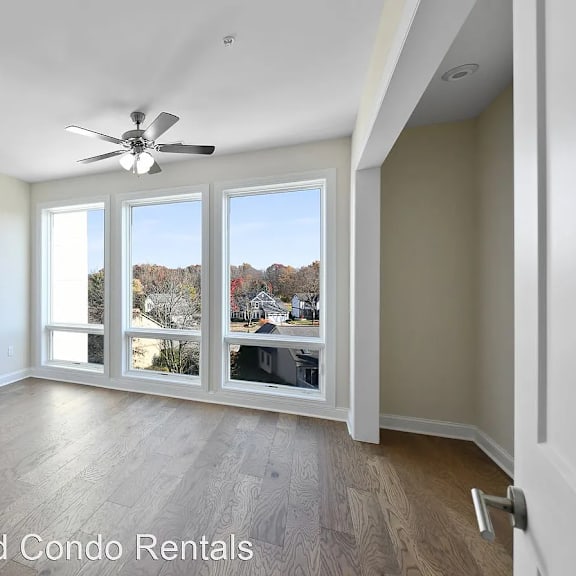 an empty living room with large windows and a ceiling fan