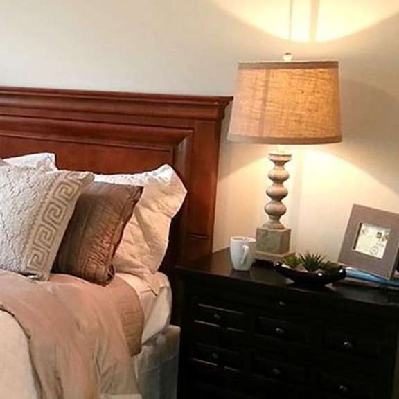 a bed with a white comforter and pillows is in a room with a lamp and a plant.