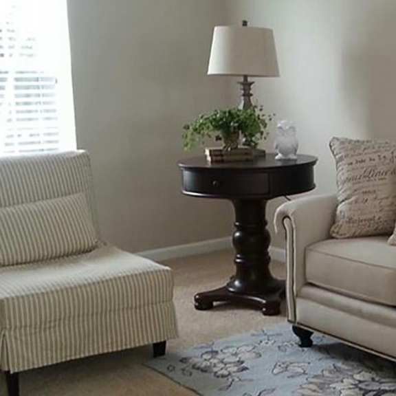 a living room with a white couch, a chair, and a table with a lamp and a plant on it.