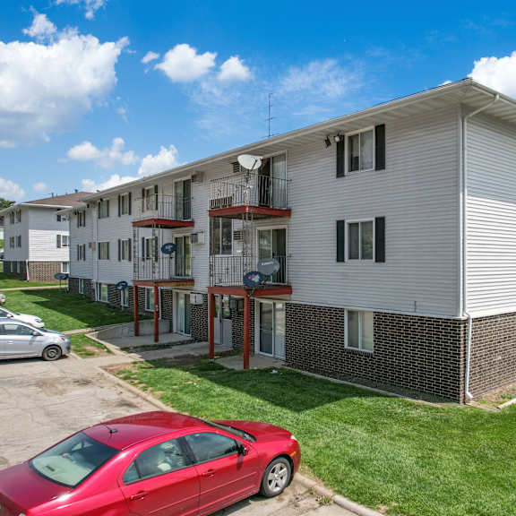 a red car is parked in front of a two-story apartment building.