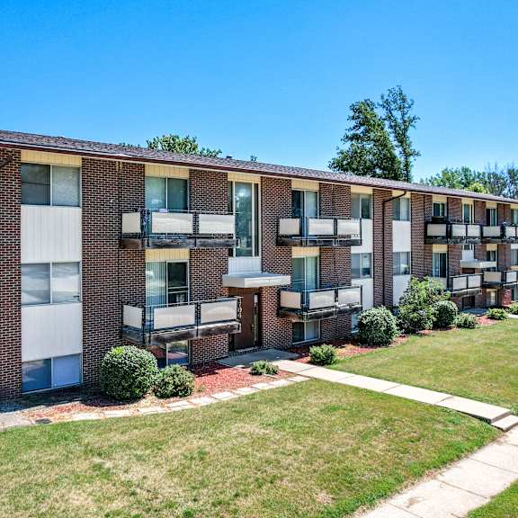 a brick apartment building with green grass and a sidewalk