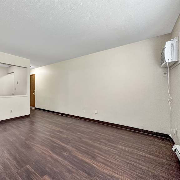 a room with a wooden floor and a white wall with a mirror and a door.