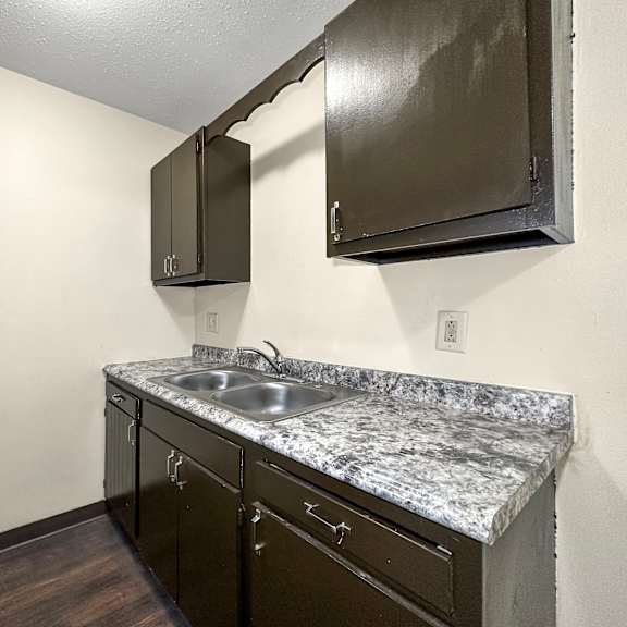 a kitchen with a granite countertop and dark brown cabinets.