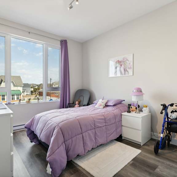 a bedroom with a purple bedspread and a view of houses outside the window.